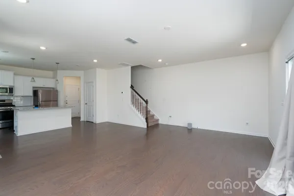 an empty room with wooden floor and a kitchen