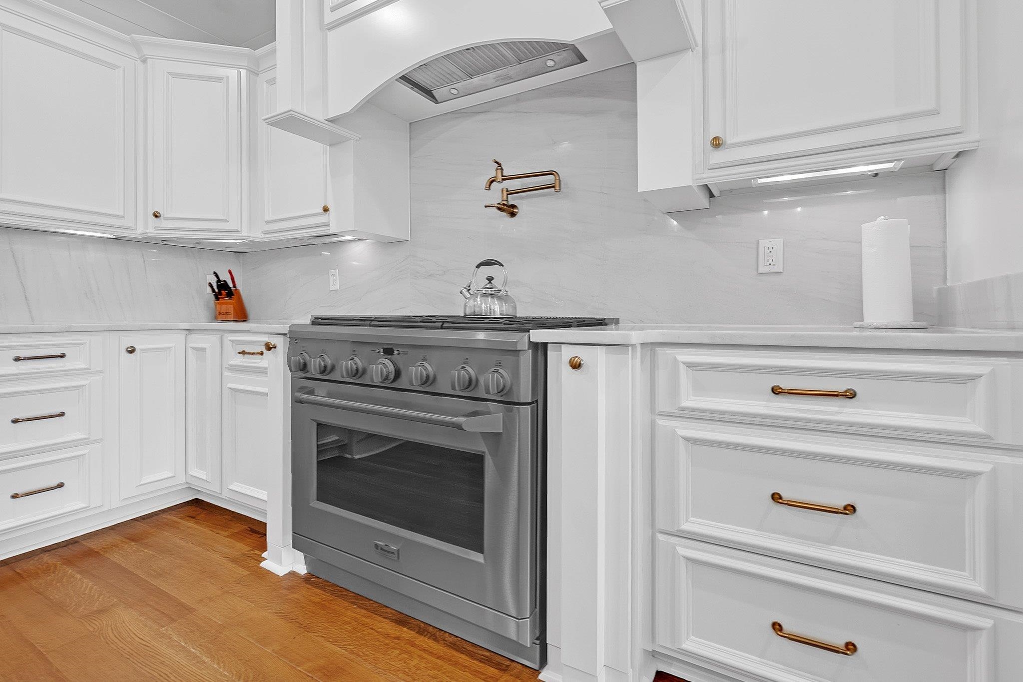 3246 North Hartwell Ridge Drive Collierville, TN 38017 - Photo 19 of 40 Professional-grade stainless steel range with a pot filler faucet, complemented by white shaker-style cabinetry, light-toned countertops, a coordinating full-height backsplash, and wood-finish flooring