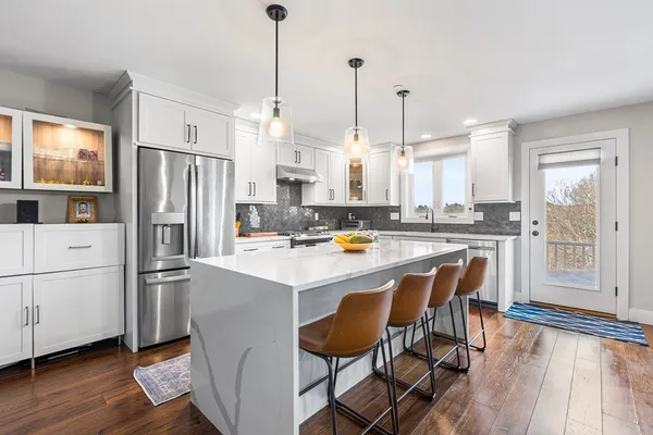 a kitchen with stainless steel appliances a stove a sink a refrigerator a center island and a wooden floor