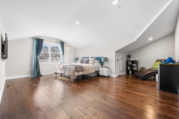 a spacious bedroom with a bed a dresser and wooden floor