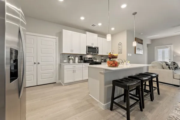 a kitchen with stainless steel appliances granite countertop a refrigerator a stove a sink and white cabinets with wooden floor