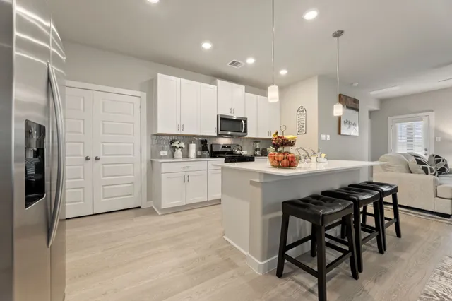 a kitchen with stainless steel appliances granite countertop a refrigerator a stove a sink and white cabinets with wooden floor