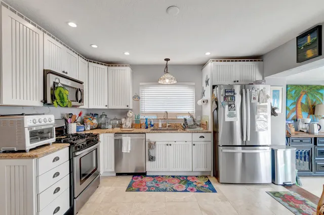 a kitchen that has a lot of white furniture a window and stainless steel appliances