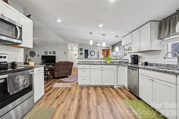 a kitchen with stainless steel appliances granite countertop a stove top oven a sink dishwasher and white cabinets with wooden floor