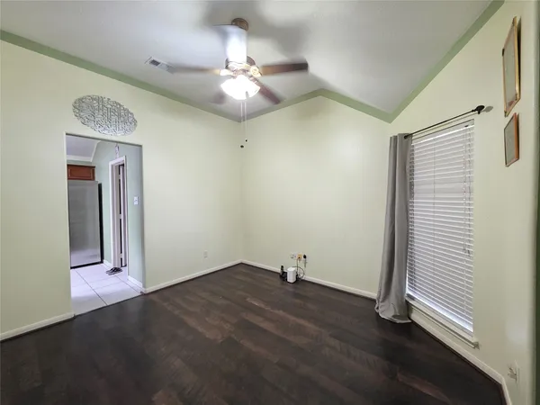 an empty room with a chandelier fan and wooden floor