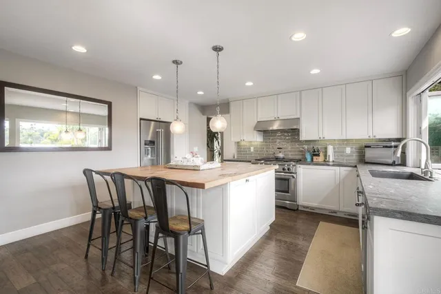 a kitchen with stainless steel appliances granite countertop a stove top oven a sink dishwasher a dining table and chairs with wooden floor