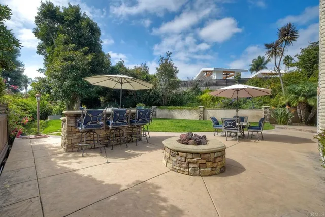 a view of a patio with a dining table and chairs under an umbrella with a fire pit and a large tree