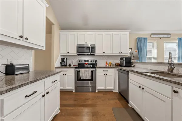 a kitchen with granite countertop white cabinets sink and stainless steel appliances