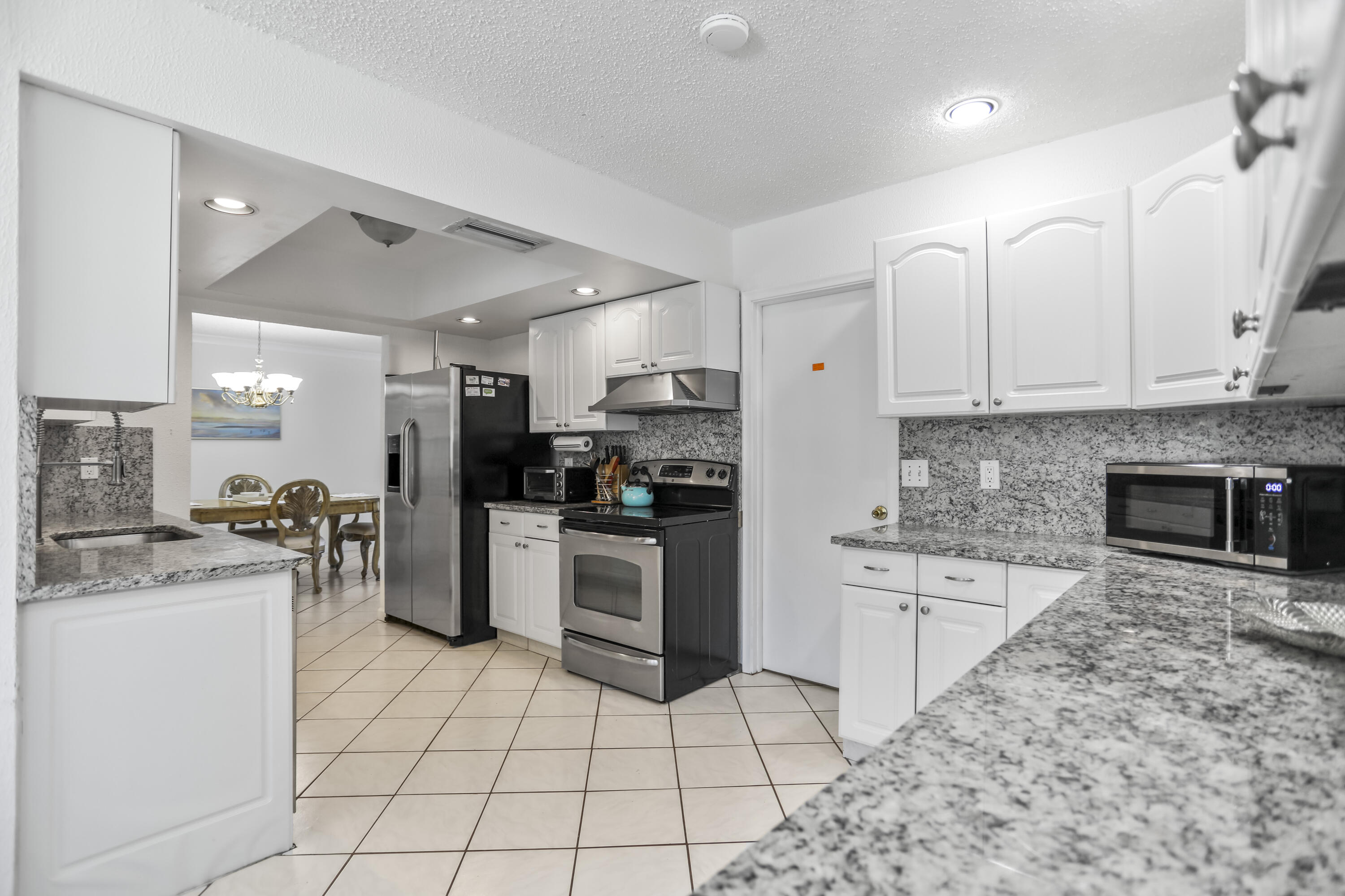 22682 Southwest 65th Avenue Boca Raton, FL 33428 - Photo 6 of 58 a kitchen with granite countertop cabinets a sink a counter space and stainless steel appliances