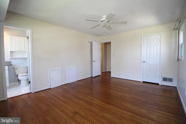a view of an empty room with wooden floor and a ceiling fan