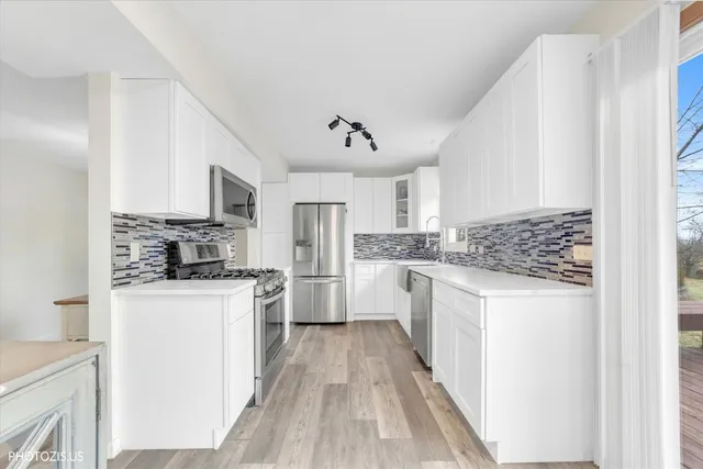 a kitchen with stainless steel appliances a refrigerator a stove a sink and white cabinets