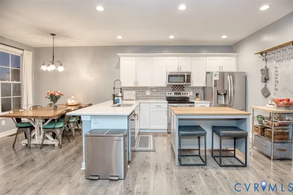 a kitchen with stainless steel appliances granite countertop a stove top oven a refrigerator a dining table and chairs with wooden floor