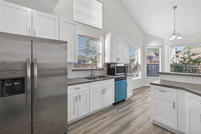 a kitchen with stainless steel appliances granite countertop a refrigerator a sink dishwasher a stove and white countertops with wooden floor