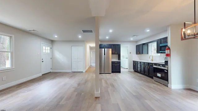 a view of an empty room with kitchen and window