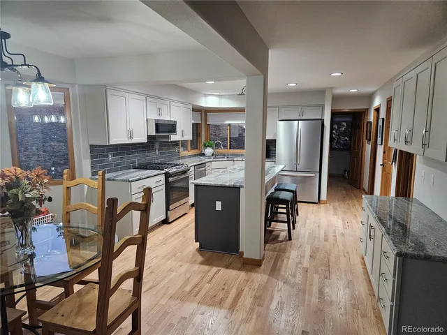 a kitchen with stainless steel appliances granite countertop a refrigerator a stove top oven a sink dishwasher and white cabinets with wooden floor