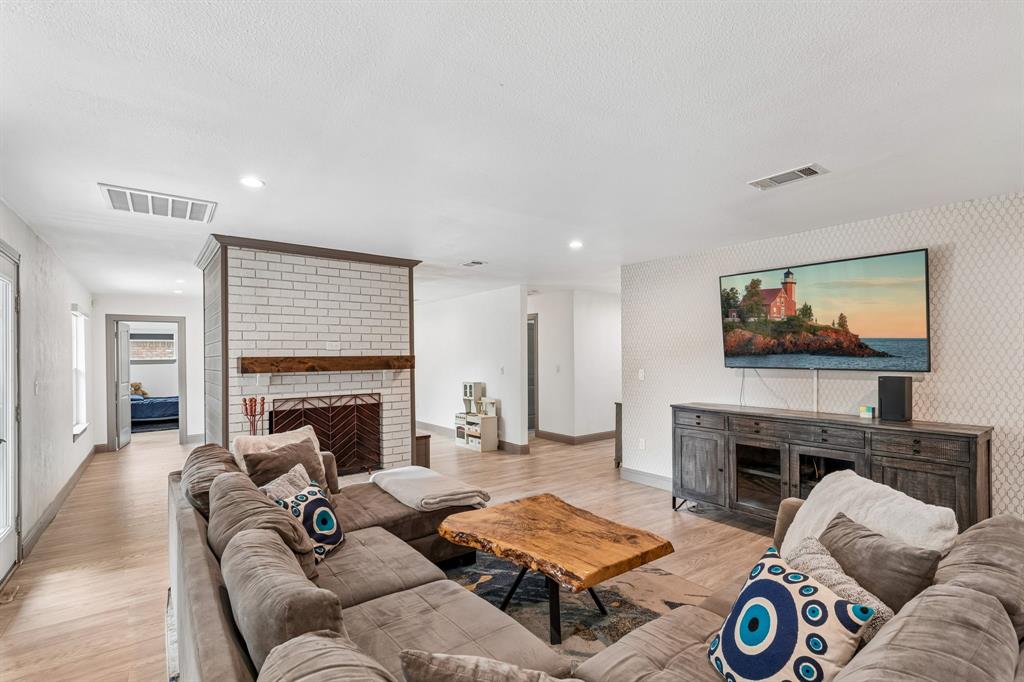 5216 Ashbrook Road Dallas, TX 75227 - Photo 2 of 28 Spacious living room featuring a brick fireplace with wood mantel, built-in cabinetry with wood-finish detailing, recessed ceiling lighting, and a wall-mounted flat-screen television above dark wood cabinetry