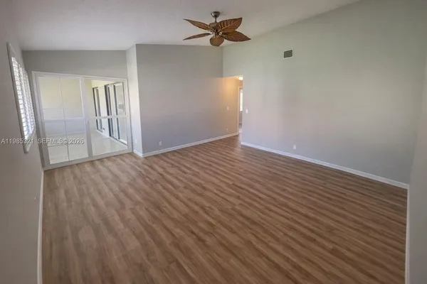 an empty room with wooden floor ceiling fan and windows