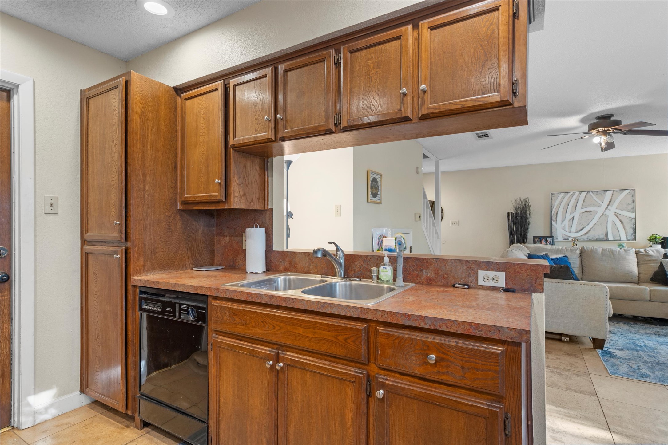 6492 Hart Lane Austin, TX 78731 - Photo 20 of 22 Kitchen with brown cabinetry, light tile patterned floors, open floor plan, black dishwasher, and ceiling fan