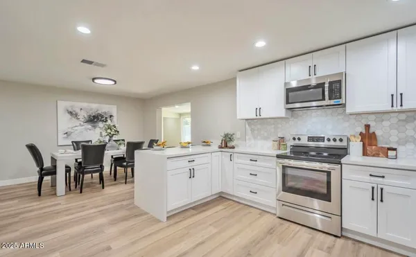 a large white kitchen with stainless steel appliances granite countertop a stove a sink dishwasher and white cabinets with wooden floor