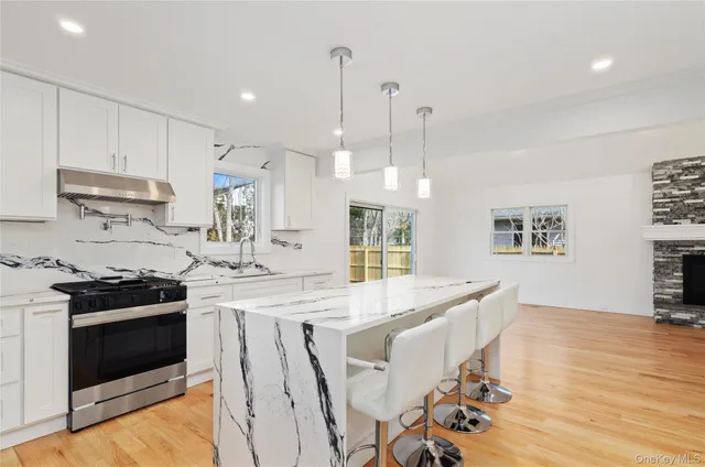 a large kitchen with granite countertop a stove a sink a refrigerator and white cabinets with wooden floor