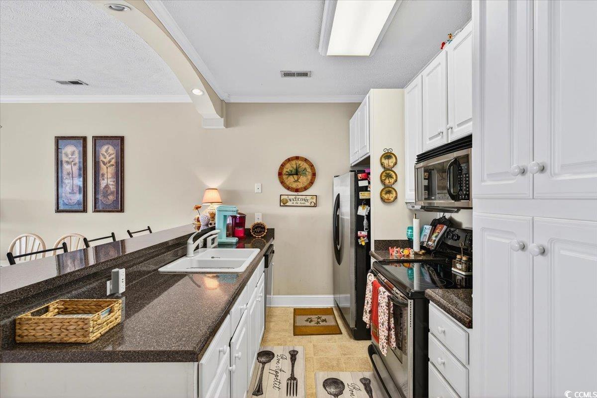 131 Waypoint Ridge Avenue, Unit 24 Little River, SC 29566 - Photo 19 of 39 Kitchen featuring appliances with stainless steel finishes, a kitchen breakfast bar, ornamental molding, white cabinetry, and a peninsula