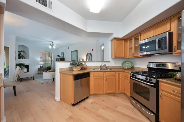 a kitchen with stainless steel appliances granite countertop a stove top oven a sink dishwasher and a microwave oven with wooden floor