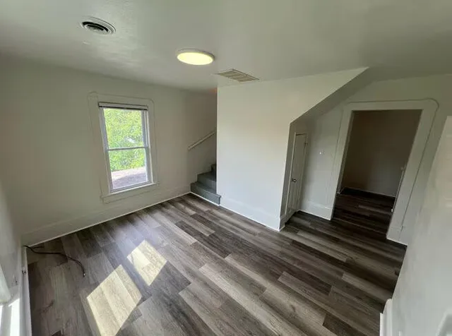 a view of an empty room with wooden floor and a window