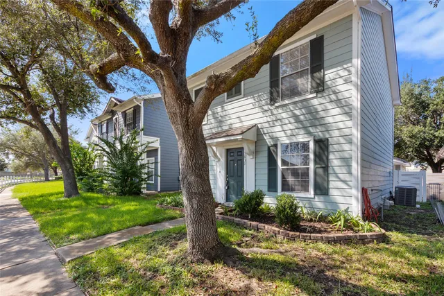 a view of a house with brick walls plants and large tree