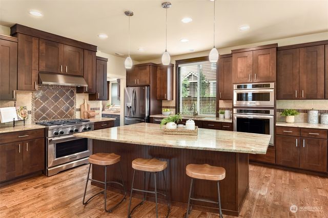 a kitchen with stainless steel appliances granite countertop a stove top oven a refrigerator a sink and a dining table with chairs