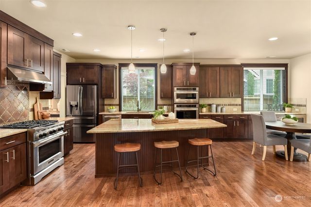 a kitchen with stainless steel appliances granite countertop a stove top oven a refrigerator a kitchen island with chairs and wooden floor