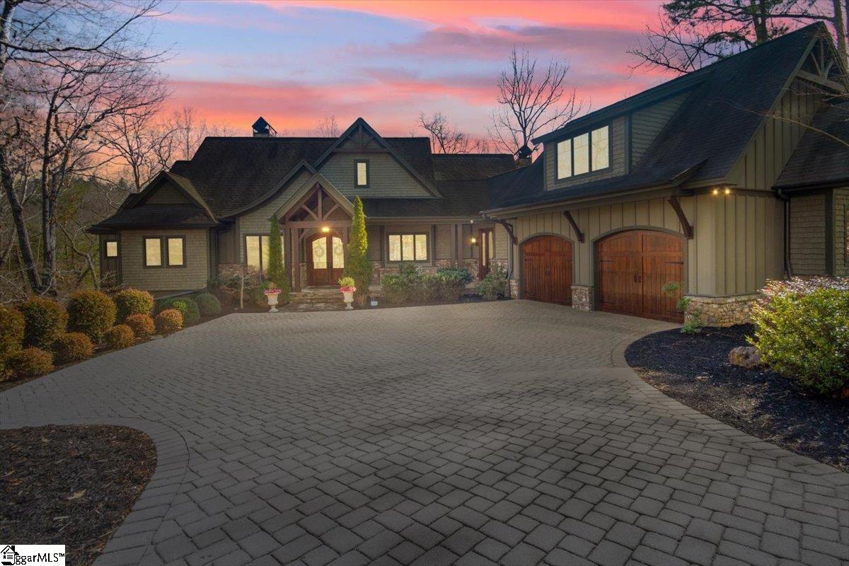206 Feather Bell Lane Sunset, SC 29685 - Photo 49 of 50 At sunset, the home’s Craftsman architecture glows under a dramatic sky, with warm interior light and a sweeping paver drive creating a striking, welcoming arrival for your dinner party.
