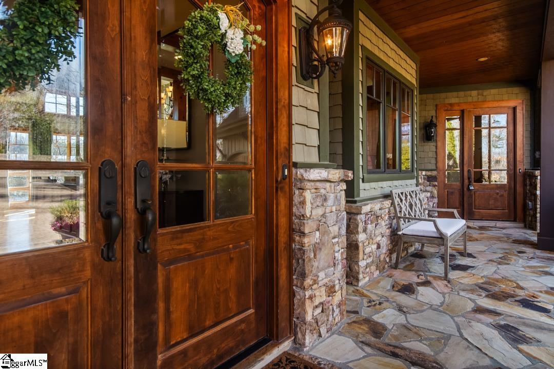 206 Feather Bell Lane Sunset, SC 29685 - Photo 5 of 50 A richly detailed covered porch with stone flooring, warm wood doors, and soft lantern light offers a gracious, inviting transition from outdoors to in.