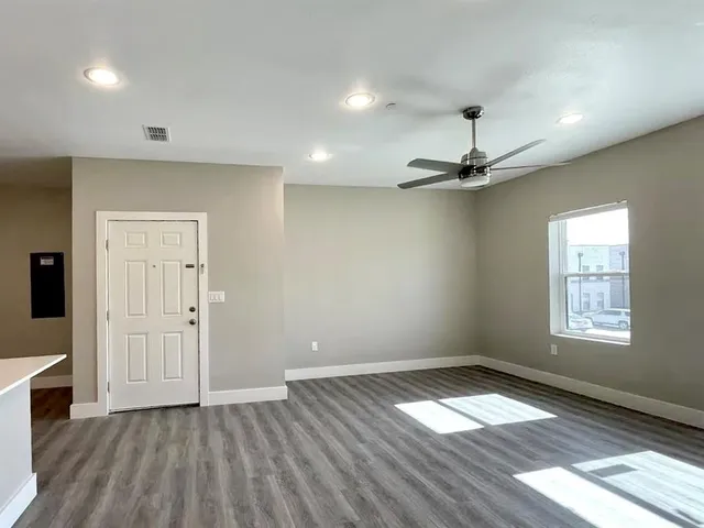 an empty room with wooden floor a ceiling fan and windows
