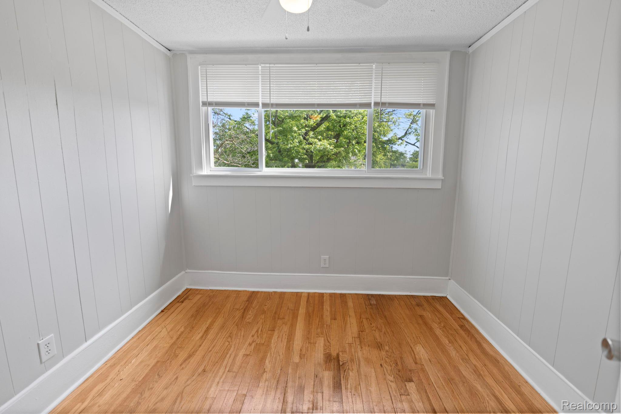 74 Pine Street River Rouge, MI 48218 - Photo 7 of 28 Unfurnished room featuring light wood-style floors, ceiling fan, and wood walls