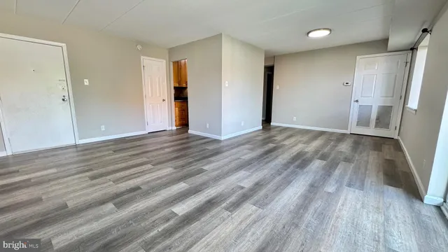 a view of an empty room with wooden floor and a refrigerator