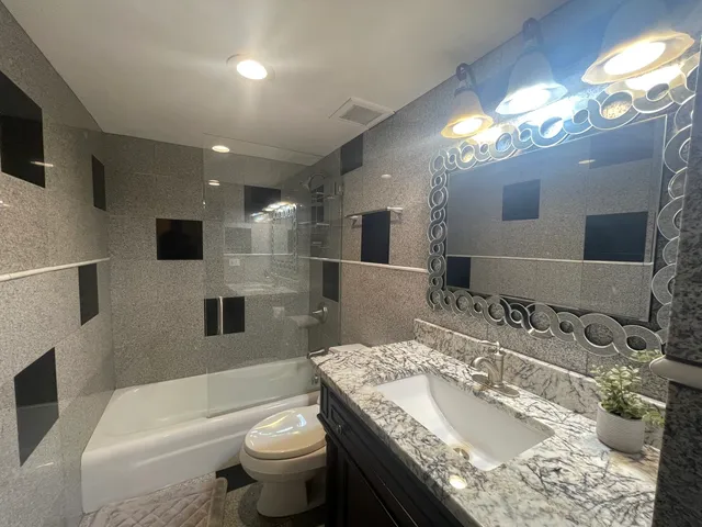 a bathroom with a granite countertop sink a toilet a mirror and shower