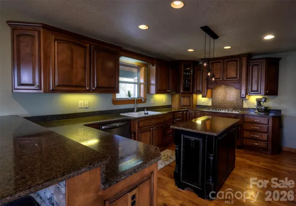 a kitchen with kitchen island granite countertop a sink dishwasher stove and cabinets with wooden floor