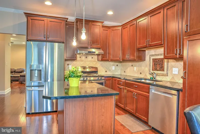 a kitchen with stainless steel appliances granite countertop a refrigerator a sink dishwasher and wooden cabinets with wooden floor