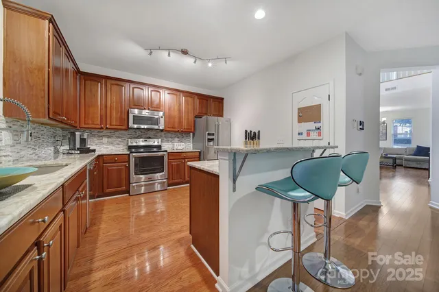 a kitchen with stainless steel appliances granite countertop a stove top oven a sink dishwasher a dining table and chairs with wooden floor