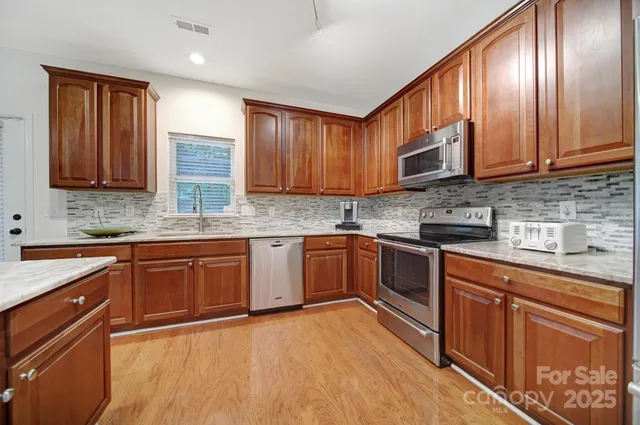 a kitchen with stainless steel appliances granite countertop wooden cabinets a sink and dishwasher a stove top oven with wooden floor