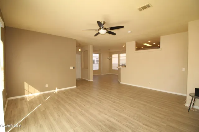 a view of an empty room with wooden floor and a ceiling fan
