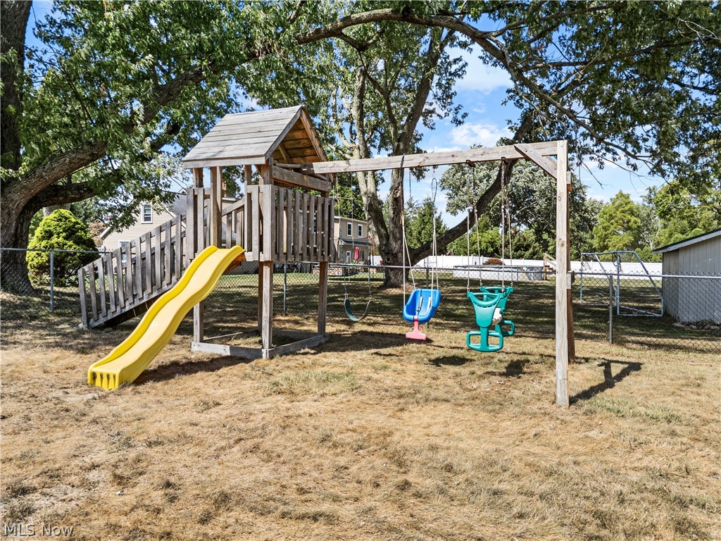 3650 Rambo Avenue Alliance, OH 44601 - Photo 31 of 36 Backyard featuring a playset with a slide and swings, mature trees, and chain-link fencing