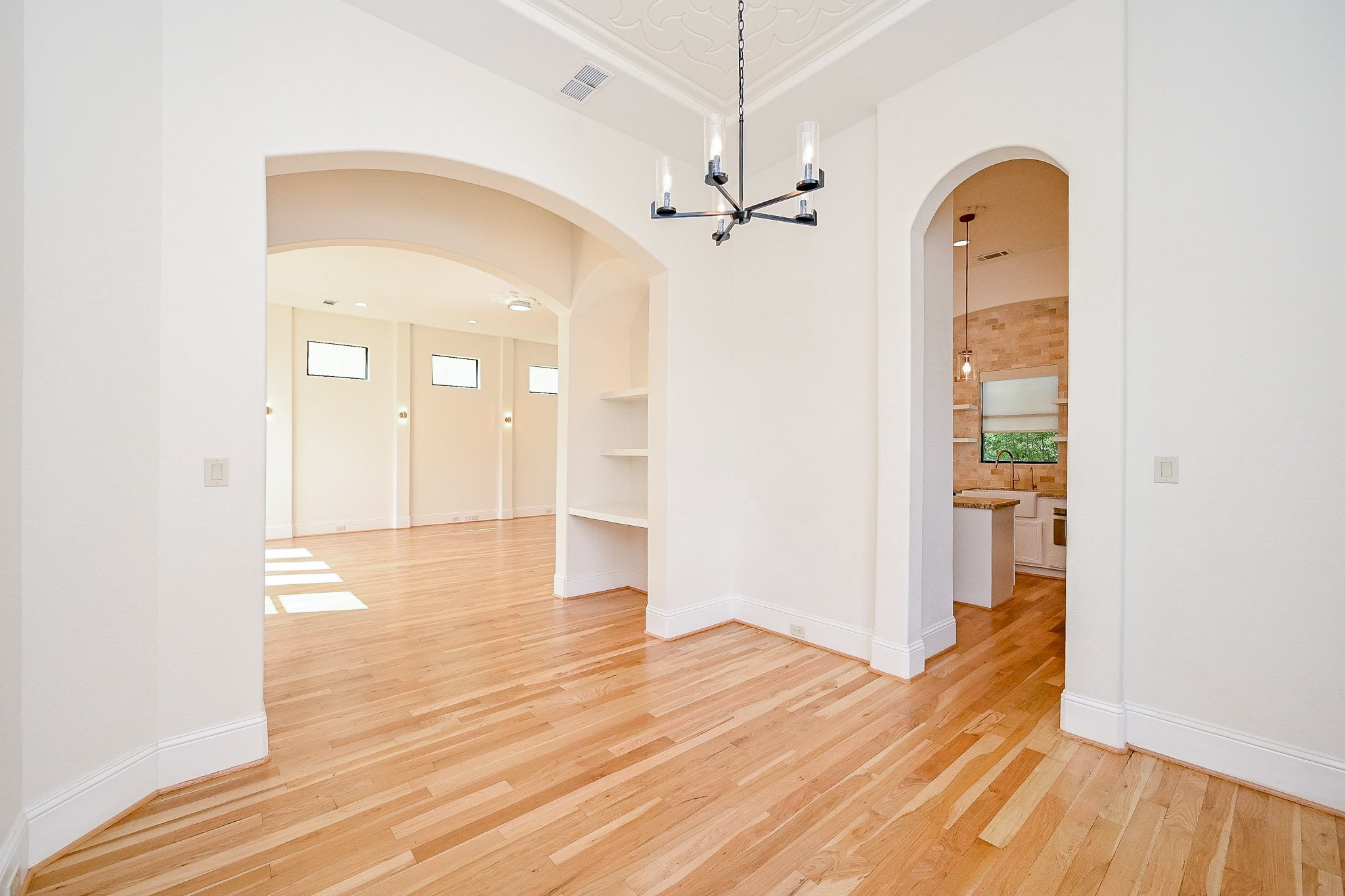 1825 West 24th Street Houston, TX 77008 - Photo 13 of 32 This bright and open space features light hardwood floors, high ceilings, and elegant archways leading to a spacious living area and a modern kitchen. A contemporary chandelier adds a stylish touch.