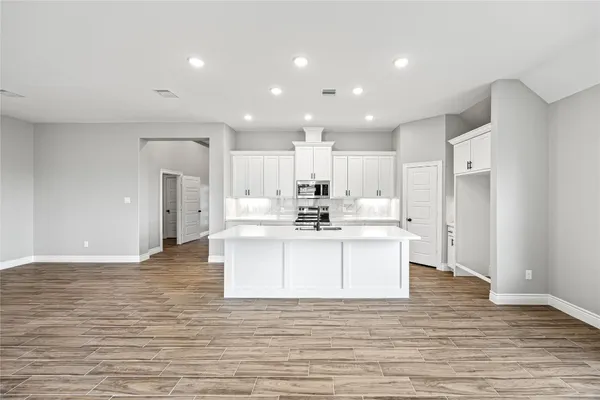 a large white kitchen with kitchen island a sink wooden floor and a refrigerator
