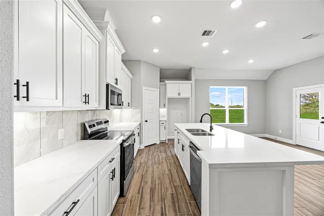 a kitchen with stainless steel appliances a stove a sink a oven a dining table and chairs with white cabinets