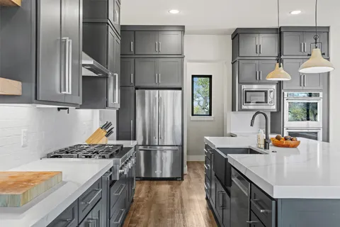 a kitchen with stainless steel appliances granite countertop a refrigerator a stove and a sink with wooden floors