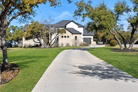 a view of a white house next to a yard with big trees