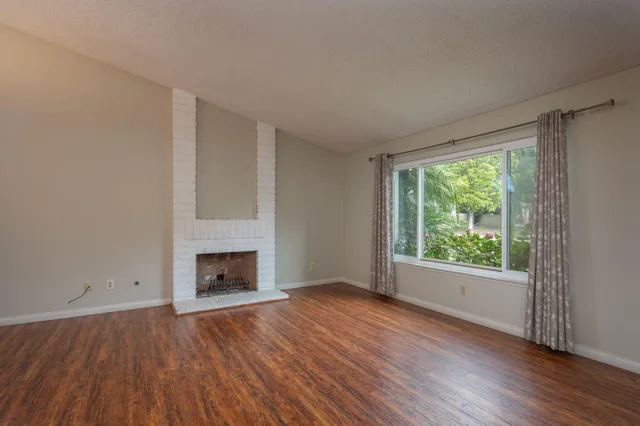 an empty room with wooden floor fireplace and windows