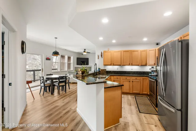 a kitchen with stainless steel appliances kitchen island granite countertop dining table chairs and a refrigerator
