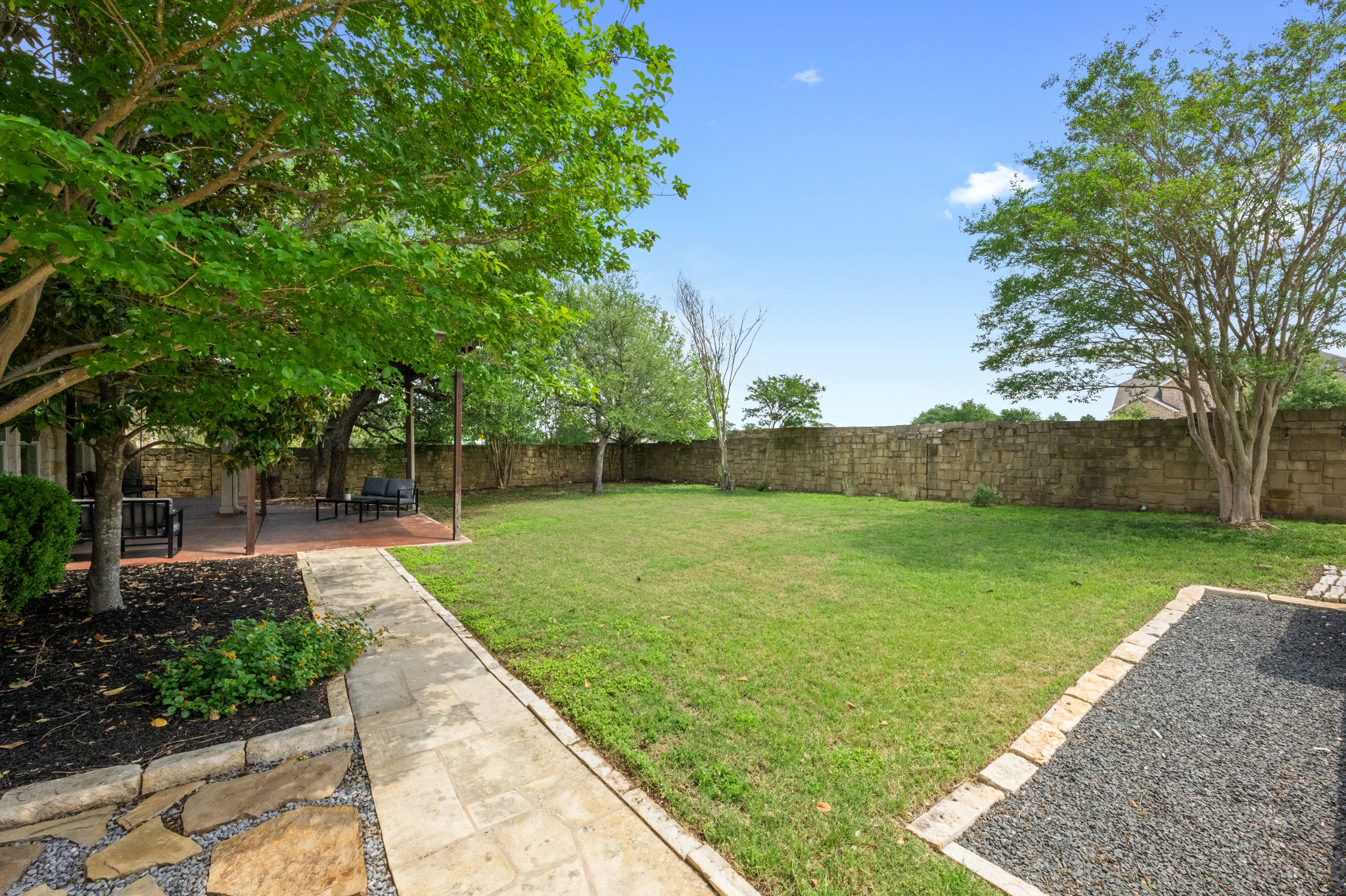 1023 Grassy Field Road Austin, TX 78737 - Photo 35 of 40 Expansive backyard featuring a stone privacy wall, a large green lawn, and mature trees
